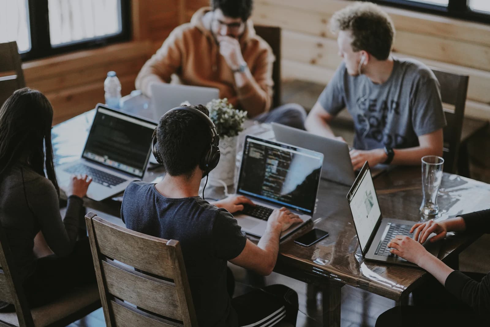 Meerdere mensen werken op laptops aan een gedeelde houten tafel