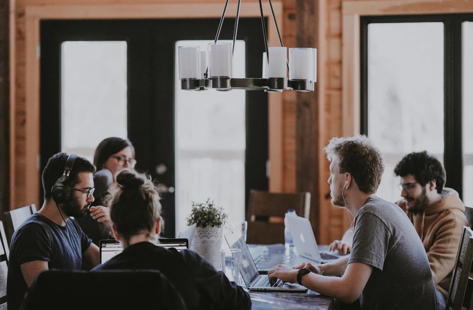 Mensen werken op laptops aan een lange tafel onder een kroonluchter