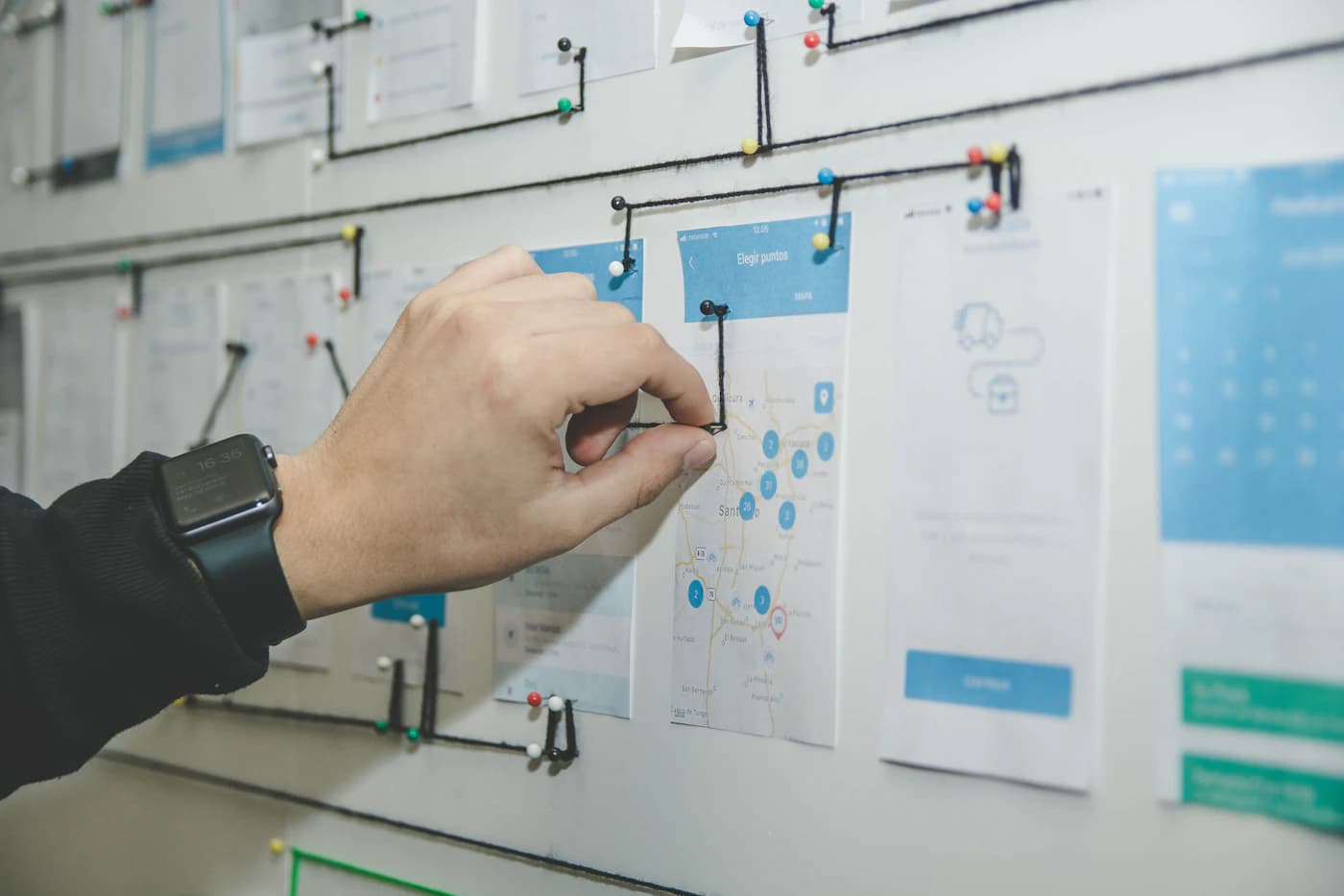 Een hand verbindt geprinte app-schermen aan een wand met zwart draad
