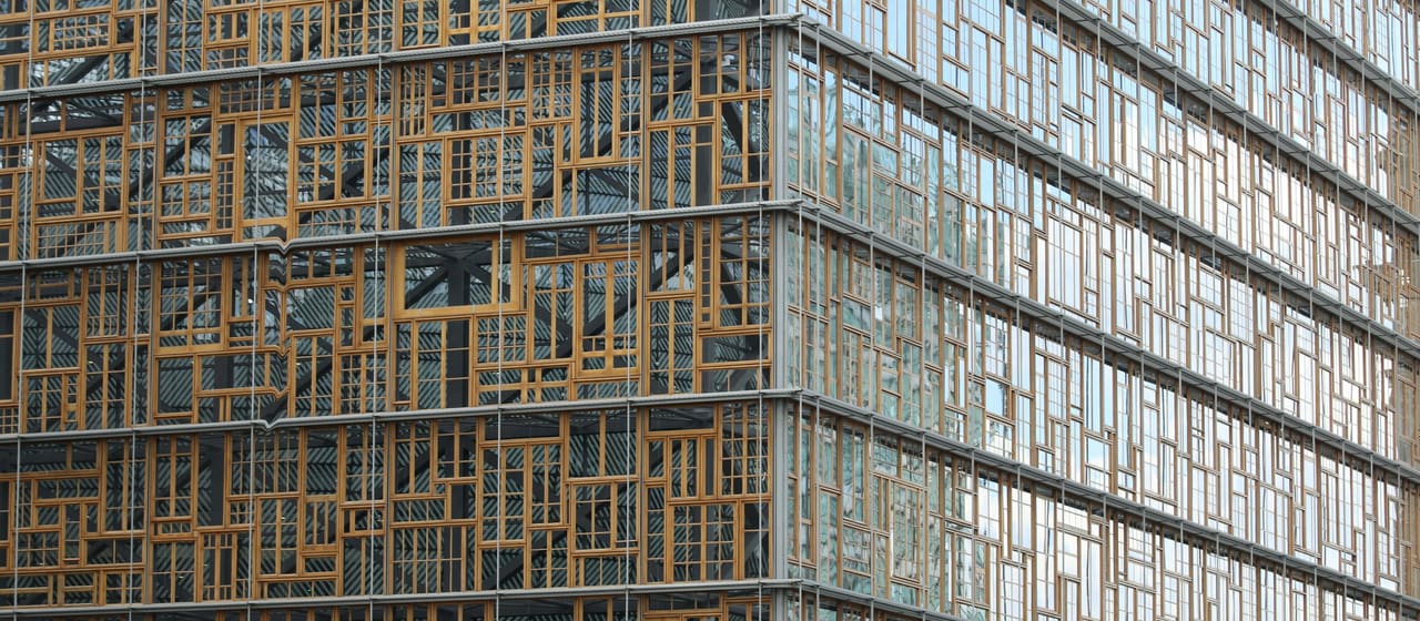 Gevel van het Europagebouw in Brussel: een raster van hergebruikte houten raamkozijnen achter een glazen huid.